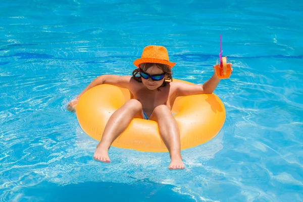 stock image Little kid boy floating in a swimming pool on summer vacation. Kid floating in pool. Child relaxing in pool, drink summer cocktail. Happy kid playing with swim ring in swimming pool