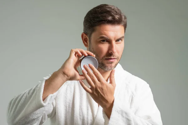 Beauty man applying cream on skin face. Handsome serious man enjoy fresh perfect skin, applying facial cream. Portrait of man with cosmetic cream on face skin. Facial treatment. Male beauty face