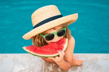 Çocuk yaz tatilinde yüzme havuzunun yanında karpuz yiyor. Çocuklar dışarıda meyve yer. Çocuklar için sağlıklı yiyecekler. Küçük çocuk bir dilim karpuzla bilardoda oynuyor.