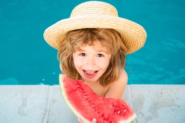 Çocuk havuzda karpuz yiyor. Kumsalda kırmızı karpuz yiyen tatlı çocuk, mavi suya karşı beyaz çocuk karpuz yiyor.