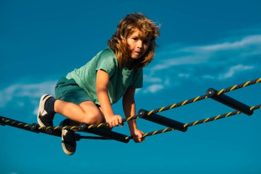 Çocuk ağa tırmanıyor. Sevimli çocuk oyun parkında merdivenleri tırmanıyor. Çocuk mavi gökyüzüne karşı merdiveni tırmanır.