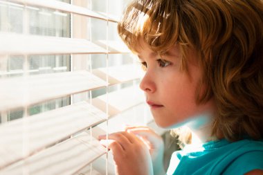 COVID-19 tecrit. Depresyondaki yalnız çocuk pencereden bakıyor. Karantina konsepti. Çocuk üzgün hissediyor. Evde tek başına kal.