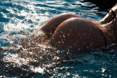 Sexy curves girl butt in bikini in pool. Sexy buttocks. Young woman shows a beautiful ass buttocks in water. Summer background