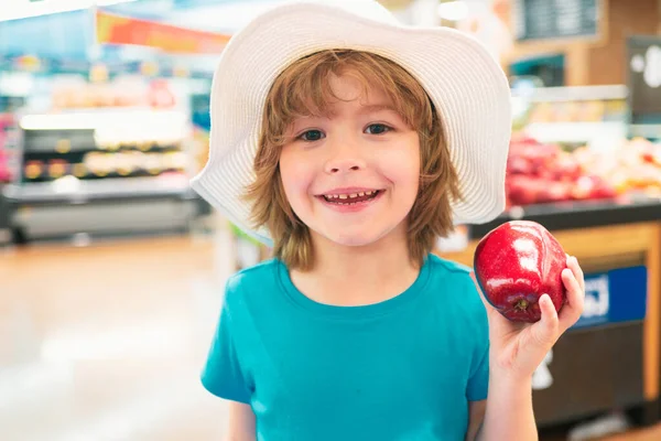 Cute toddler boy in a food store or a supermarket choosing fresh organic apple. Healthy lifestyle for young family with kids. Sale, consumerism and kids concept