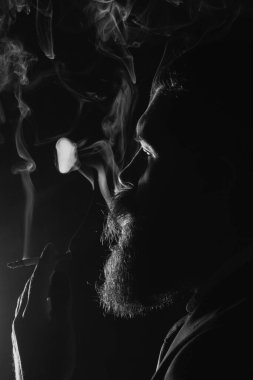 Sigara içen sakallı adamın yakın portresi. Siyah arka planda sigara dumanı