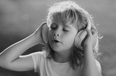 Şarkı söyleyen çocuklar. Kulaklıklı genç çocuk müzik dinliyor, açık havada gözleriyle favori müziğin tadını çıkarıyor.