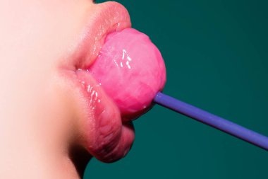 Ağzında lolipop var, yakın plan. Ağzında lolipop olan güzel bir kız. Dili parlak kırmızı kadın dudakları. Ağız yalamak chupa chup emmek