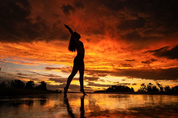 Black silhouette of pretty girl or beautiful woman, sexy slim model, with long hair poses on sea beach at sunset outdoors on yellow sky background