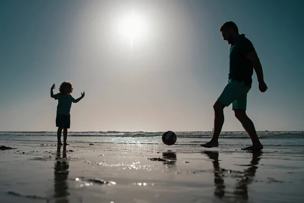 父と息子は夏休みにビーチでサッカーやサッカーをします 父と子供が屋外で遊ぶ 日没のシルエット — ストック写真