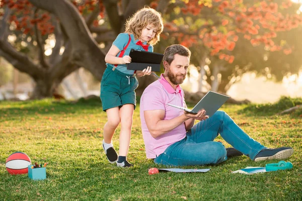 Happy child with father learning outdoor by studying online and working on laptop