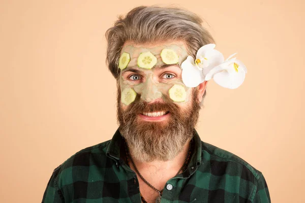 Funny man with clay mask and cucumber slices on face. Spa, dermatology, wellness and facial treatment concept. Man having cosmetic moisturizing mask, isolated studio background. Male face care