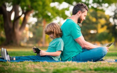 Baba oğul park yerinde dizüstü bilgisayarı var. Babam çocuklara modern teknolojiyi kullanmayı öğretiyor. Mesafe öğrenme dersi. Okul eğitimi