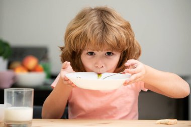 Lezzetli yulaf lapası yiyen, evde sütlü mısır gevreği yiyen, mutfaktaki masada oturan küçük sevimli çocuğun yakından çekilmiş yüzü. Anaokulu çocuğu sabah kahvaltısının tadını çıkarıyor.