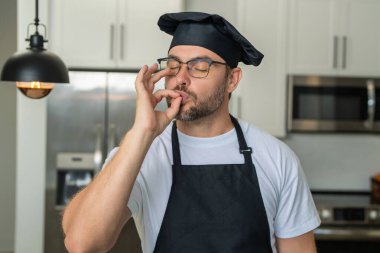 Aşçı fırıncının yakın portresi, fırıncı. Mükemmel yemek alameti olan erkek şefler. Şef yemek pişiriyor, lezzet işareti yapıyor. Şef, aşçı parmaklarını öperek lezzetli bir jest yapıyor.