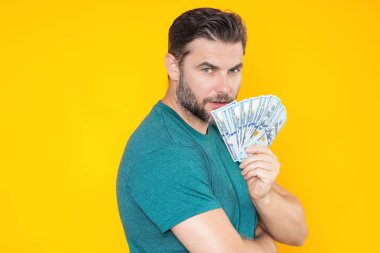 İyi ödeme. Yakışıklı adam gri stüdyoda izole edilmiş para tutuyor. Dolar banknotları halinde para. Yığınla para, finans, yatırım ve tasarruf