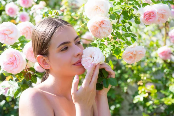 stock image Beautiful girl smelling a rose flower in spring park. Young woman in flowering garden with roses. Beauty model with spring flowers. Happy spring. Pretty woman enjoying smell flowers in spring park