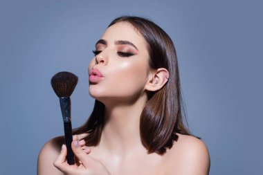 Studio portrait of a woman applying cosmetic tonal foundation on face using makeup brush. Beautiful girl doing contouring apply blush on cheeks isolated on studio background