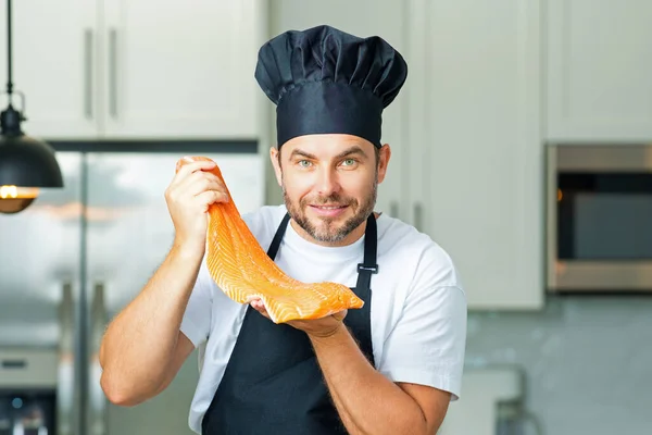 キッチンで魚のサーモンを調理するハンサムな男 鮭の魚とキッチンでカジュアルな男の料理の肖像画 カジュアルな男は台所で生の魚サーモンを準備 大きなサーモンステーキのシェフ — ストック写真