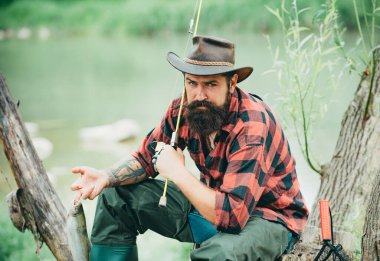 Hobi yaparken balık tutan adam dinleniyor. Erkek hobisi. Hobilerin evi. Balık avlama maceraları. Nehirde balık tutan neşeli, olgun bir balıkçı. Sakallı zarif adam. Balıkçı balık yakalıyor.