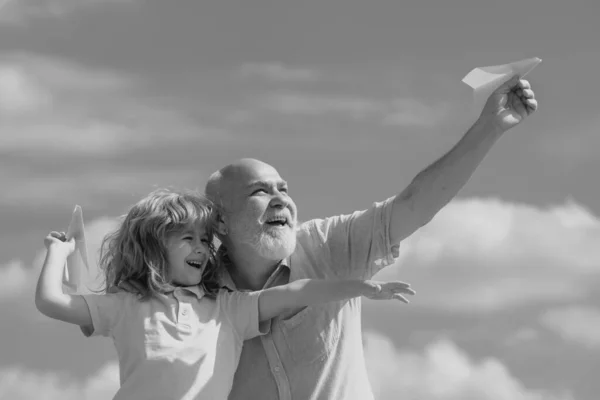 年轻的孙子和老爷爷带着玩具纸飞机 在夏日的天空背景下 梦想着飞翔的小男孩 — 图库照片