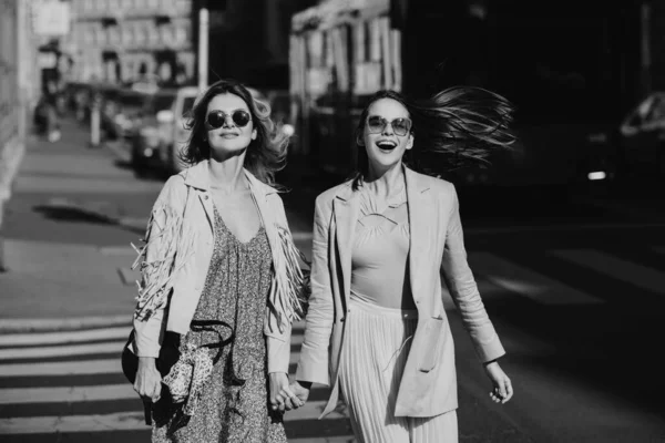 かなりの女の子が屋外で通りを歩いて楽しんでいます 最高のガールフレンド 都市のスタイル ２人の友人が街の中心部でサングラスをかけて笑って歩く — ストック写真