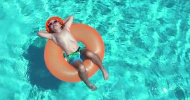 Yaz eğlencesi. Havuzda yüzen küçük tatlı bir çocuk. Havuzdaki çocuğun yukarıdan görünüşü, gevşeme, şişme halkada yüzme. yaz tatili konsepti