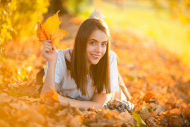 Sonbahar mevsimi. Yaprakları yapraklı genç bir kadının portresi. Sonbaharda güzel bir kız. Sonbaharda sarı yapraklı şehvetli bir kadın. Sonbahar arkaplanında yaprağı olan güzel bir kadın.