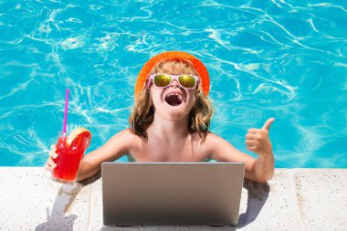 Çocuk yaz kokteyli içer ve havuzda dizüstü bilgisayar kullanır. Çocuk yüzme havuzunda dizüstü bilgisayarla çalışıyor. Seyahat turizmi ve iş konsepti. Yaz günlüğü