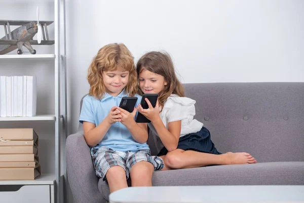 2人の子供だけで自宅で電話 子供たちの友人や友情 自宅でスマートフォンを持つ小さな子供たち ソファに座っている間にスマートフォンを使用して子供たち スマートフォンで遊ぶ子供たちの肖像 — ストック写真