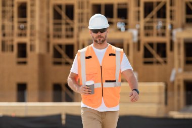 Amerikan ahşap bina inşaatında kahve molası vermiş miğferli bir inşaatçı. İnşaat alanında miğferi olan bir işçi. Bilder in hardhat