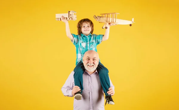Child boy and grandfather playing piggyback ride with plane and wooden toy truck. Men generation granddad and grandchild. Elderly old relative with child