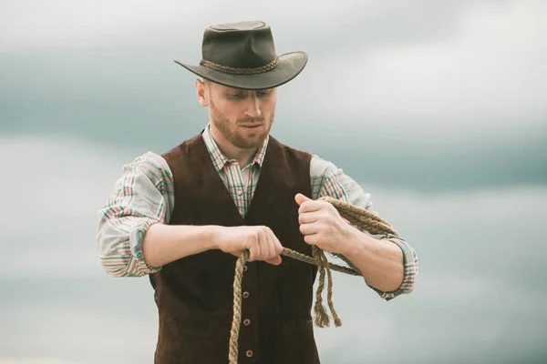 American cowboy man. Handsome brutal western guy. Cowboy with lasso rope on  sky background. Photos