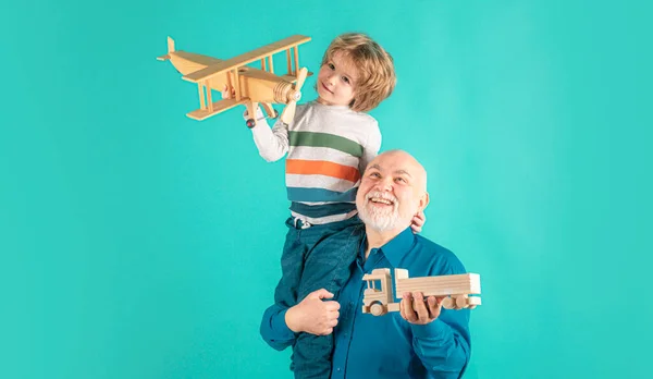 Young grandson and old grandfather piggyback with toy plane and wooden truck. Men generation granddad and grandchild