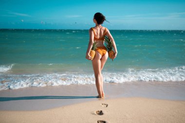 Sporty back with sexy butt of a beautiful woman in bikini with a pineapple on ibiza or miami sea background with copyspace. Sexy female buttocks on summer beach