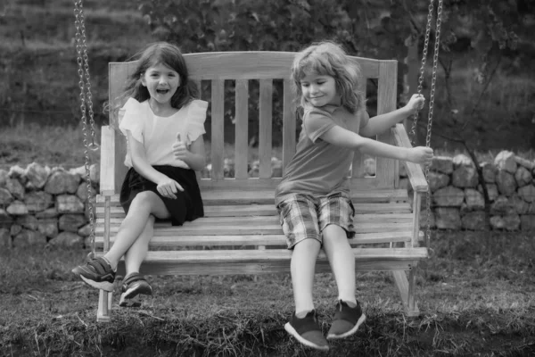 屋外で揺れる2人の子供 屋外でスイングに座っている間 愛らしい兄と妹の笑顔と笑いの肖像画 幸せなライフスタイルの子供 — ストック写真