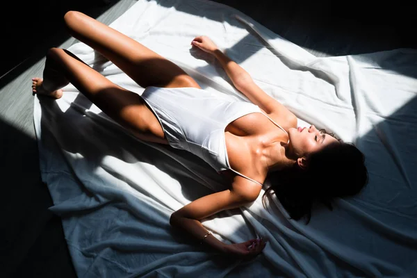 ボディスーツモデル ベッドでセクシーな女性セクシーランジェリー セクシーな水着姿の若い官能モデルがベッドに横たわっています 女の子はベッドで休んでいる 白いベッドの上にポーズをとるセクシーな女性 高級ランジェリー スリムな官能的な体 — ストック写真