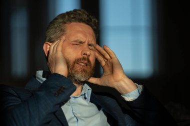 Baş ağrısı çeken yorgun bir adam. Başa dokunmak, ağrıyı dindirmek, migren. İş sorunları. İflas, mali sorun ve kriz konsepti. Bin yıllık İspanyol adamın başı ağrıyor. Migren.