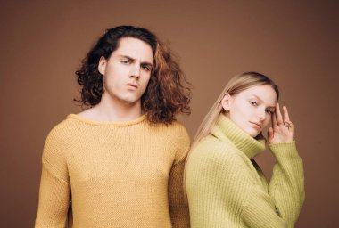 Stüdyoda bej arka planda moda bir çift. Kıvırcık saçlı bir çift adam ve kuaför salonunda sarışın bir kadın. Vogue tarzı. Gençlik, aşk ve yaşam tarzı konsepti