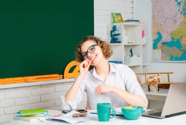 Masasındaki kadın öğretmen öğrencilerin çalışmasını onaylıyor. Güzel öğretmen okulda kameraya gülümsüyor. Üniversite öğrencisi