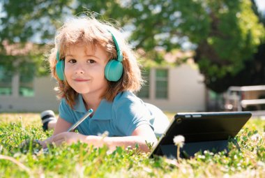 Çocuk mesafesi öğrenme konsepti. Uzaktan eğitim, okul parkında online ders alan bir çocuk. Kalemle kitap yazan bir öğrenci, açık havada çalışmaz. Kendi kendine öğrenim öğrenme. Erken gelişim