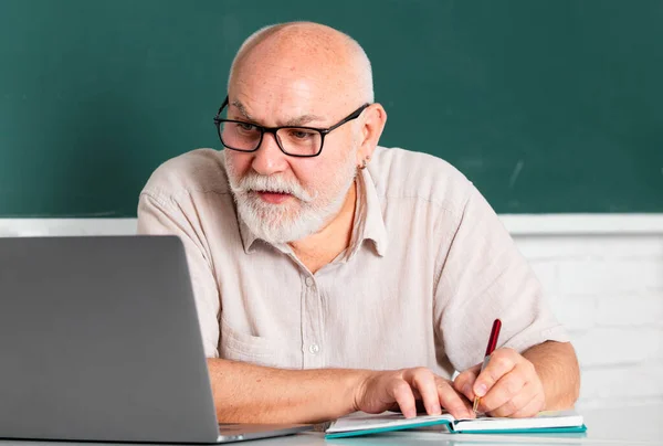 老年教育和退休知识概念 高级教师在教室里用黑板授课 大学老师 高级男教师在教室里用笔记本电脑坐在课桌前 — 图库照片