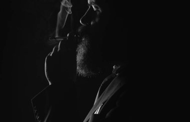 Siyah arka planda sigara içen genç adamın yüzünde koyu bir gölge var. Sigara içen adam