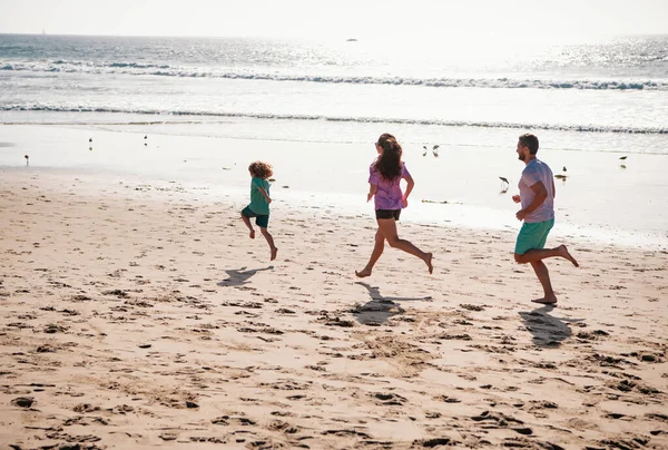 幸せな家族の父 母と赤ちゃんの息子が屋外で一緒にジョギングし 黒い砂のビーチで海の波に沿ってウォータープールで運営されています 夏休みに子供と一緒に旅行ライフスタイル — ストック写真