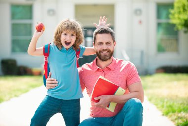 Öğretmenler günü. Amerikan baba ve oğlu okul parkında yürüyor. Okul bahçesinde mutlu bir aile