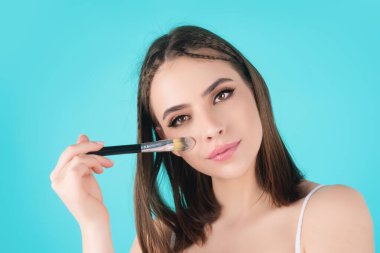 Beautiful young woman apply powder on face. Beauty Makeup. Portrait of female model with cosmetic brush. Perfect soft skin and natural makeup. Applying powder blush highlighter, foundation tone