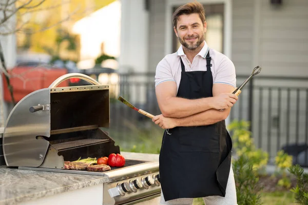 男性シェフは庭でグリルし バーベキューをします バーベキュー屋外ガーデンパーティー バーベキューの肉を準備するハンサムな男 夏の間の屋外での食事と料理の概念 — ストック写真