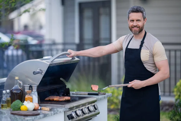 明るい若い男がバーベキュー屋外で肉を焼くの肖像画 ローストやグリル料理 肉を屋外で焙煎する バーベキューとグリル 裏庭で肉を調理 — ストック写真