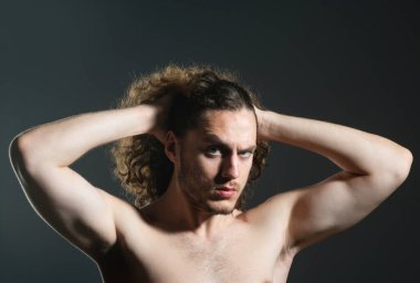 Kıvırcık saçlı adam. Sağlıklı kıvırcık saçlar, yakışıklı, maço, yakışıklı ve uzun kıvırcık saçlı, gri arka planda yalnız bir adamın yakın portresi. Erkek modern saç kesimi