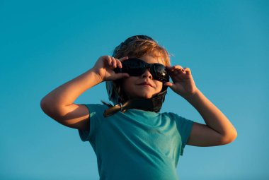 Pilot gözlüklü ve kasklı küçük çocuk pilot ve astronot olmak istiyor. Mutlu çocuk gökyüzünde oynuyor. Çocuklar uçmayı hayal eder.