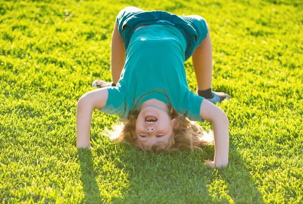 stock image Happy kid boy girl standing upside down on her head on grass in summer day